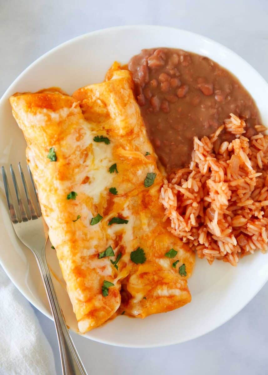 Cheese enchiladas with rice and beans on a plate.