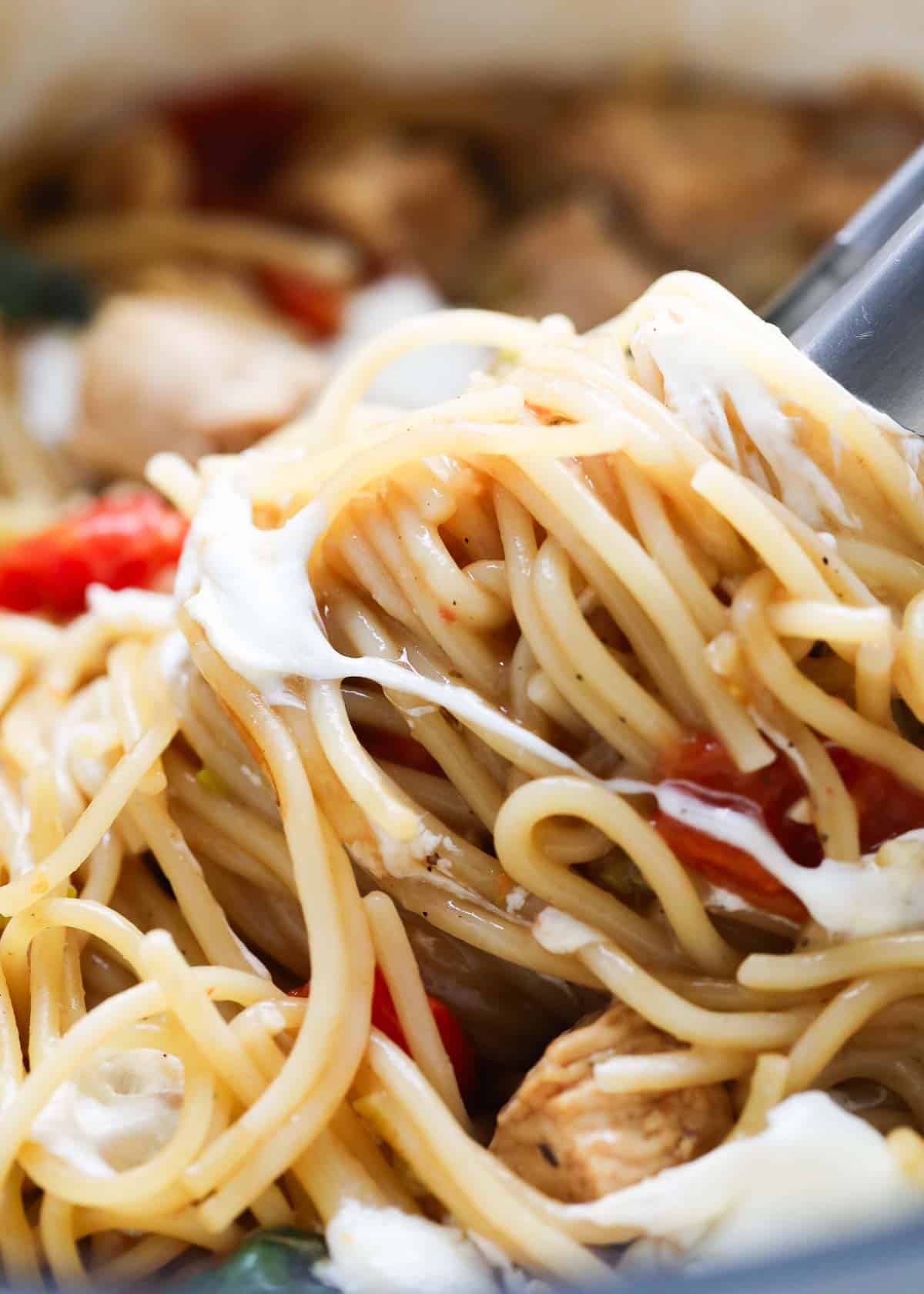 Up close caprese chicken pasta with tongs swirling the pasta around. 