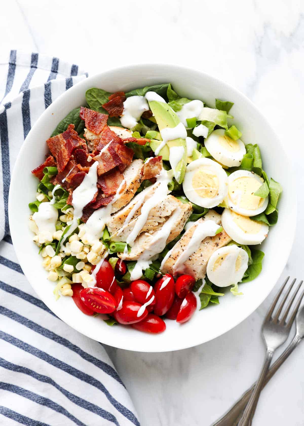 Cobb salad in a white bowl drizzled with dressing. 