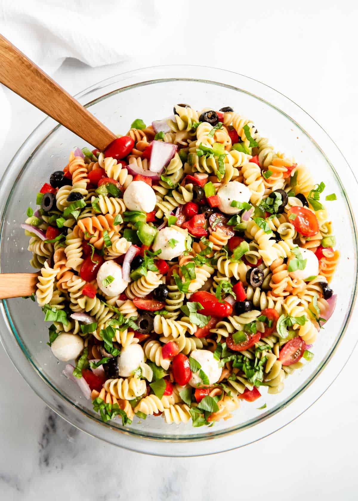 Easy pasta salad with Italian dressing in a glass bowl with wooden spoons for serving.
