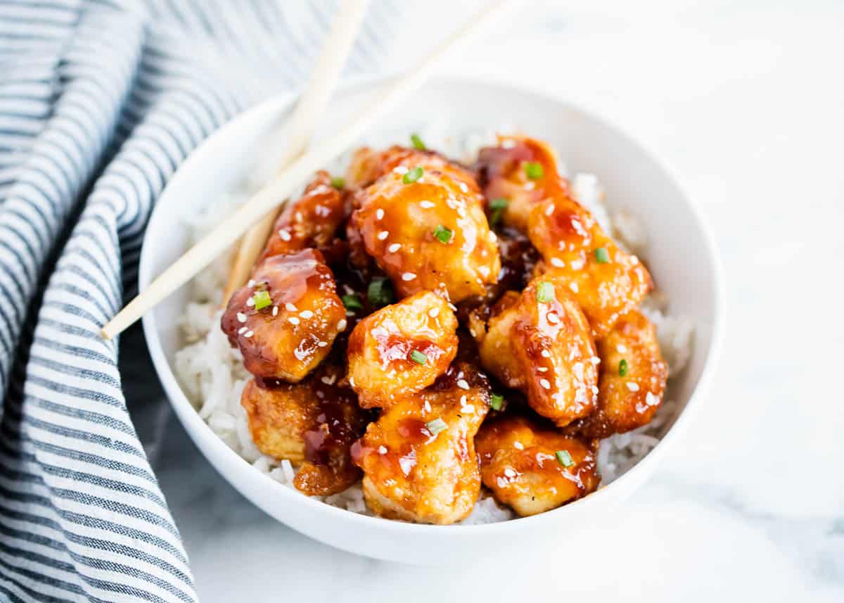 Skip the takeout and make this delicious General Tso's chicken at home! You'll fall in love with the sweet and spicy sauce poured over the crispy, juicy chicken. This is truly a restaurant-style recipe! General Tso's chicken in a white bowl with chopsticks on the side.
