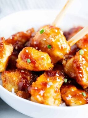 Tender chicken pieces coated in sticky sweet-and-savory sauce, garnished with sesame seeds and green onions.