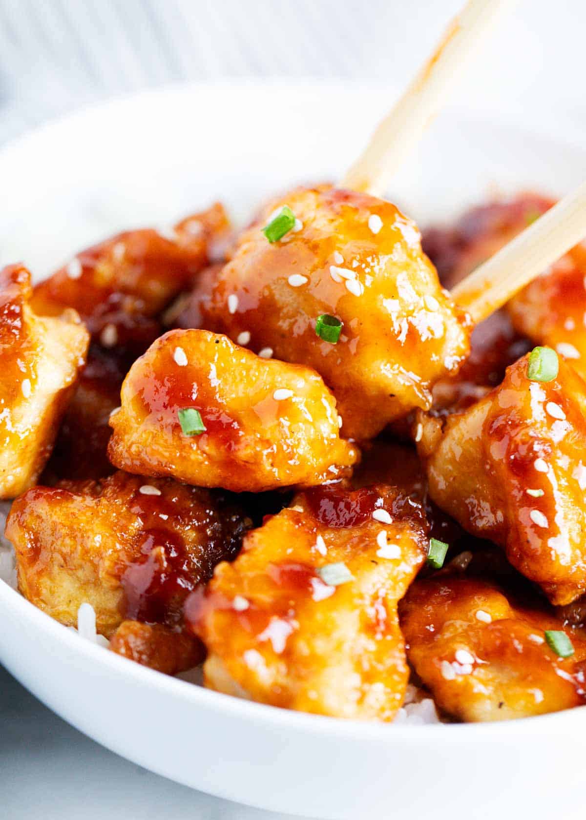 General Tso's chicken in a white bowl up close photo with chopsticks. 