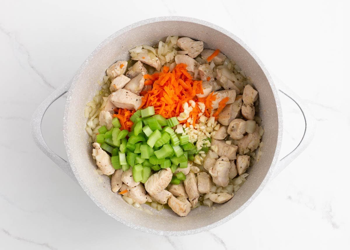 Diced onion, celery, shredded carrot, and garlic added to the pot with cooked chicken.