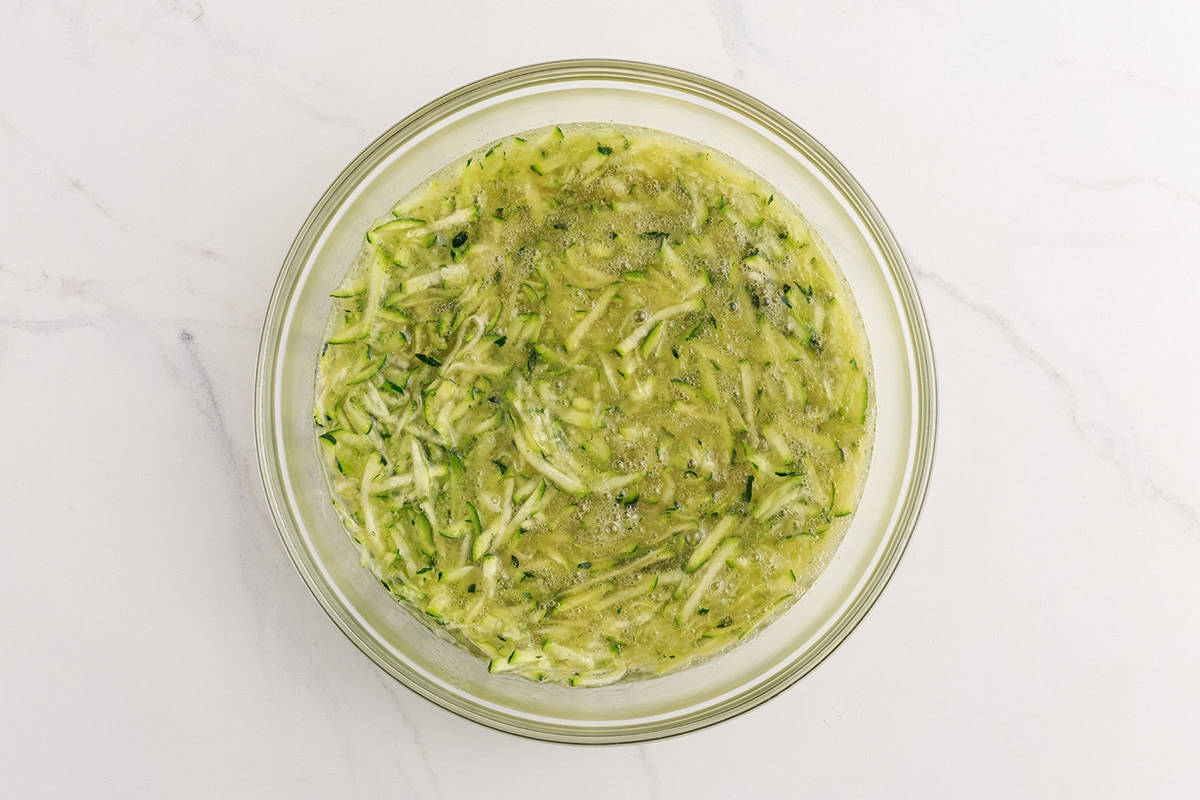 Shredded zucchini in a bowl with wet ingredients for muffin batter. 