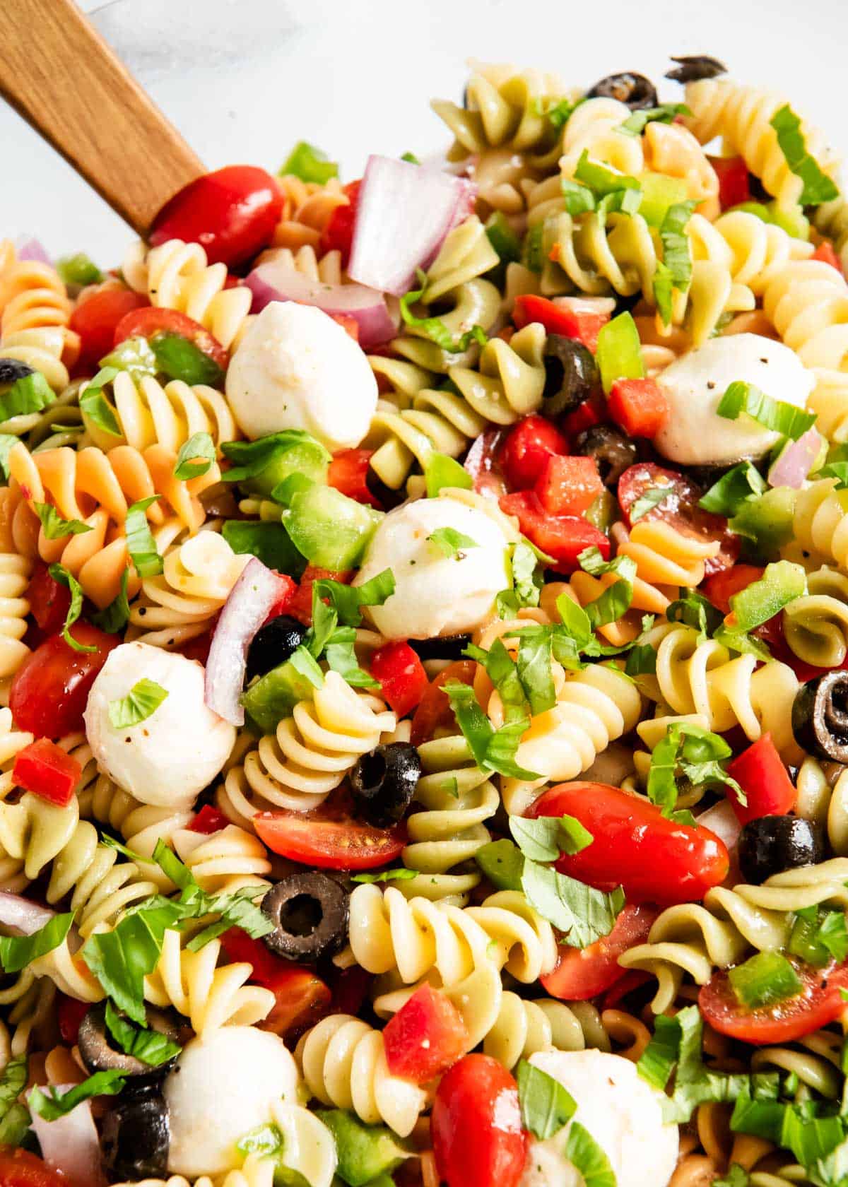 Pasta salad tossed together with Italian dressing using wooden spoons. 