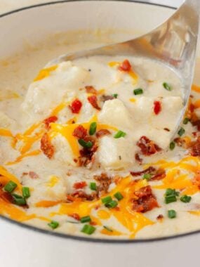 Loaded baked potato soup being served from a pot with a soup ladle.