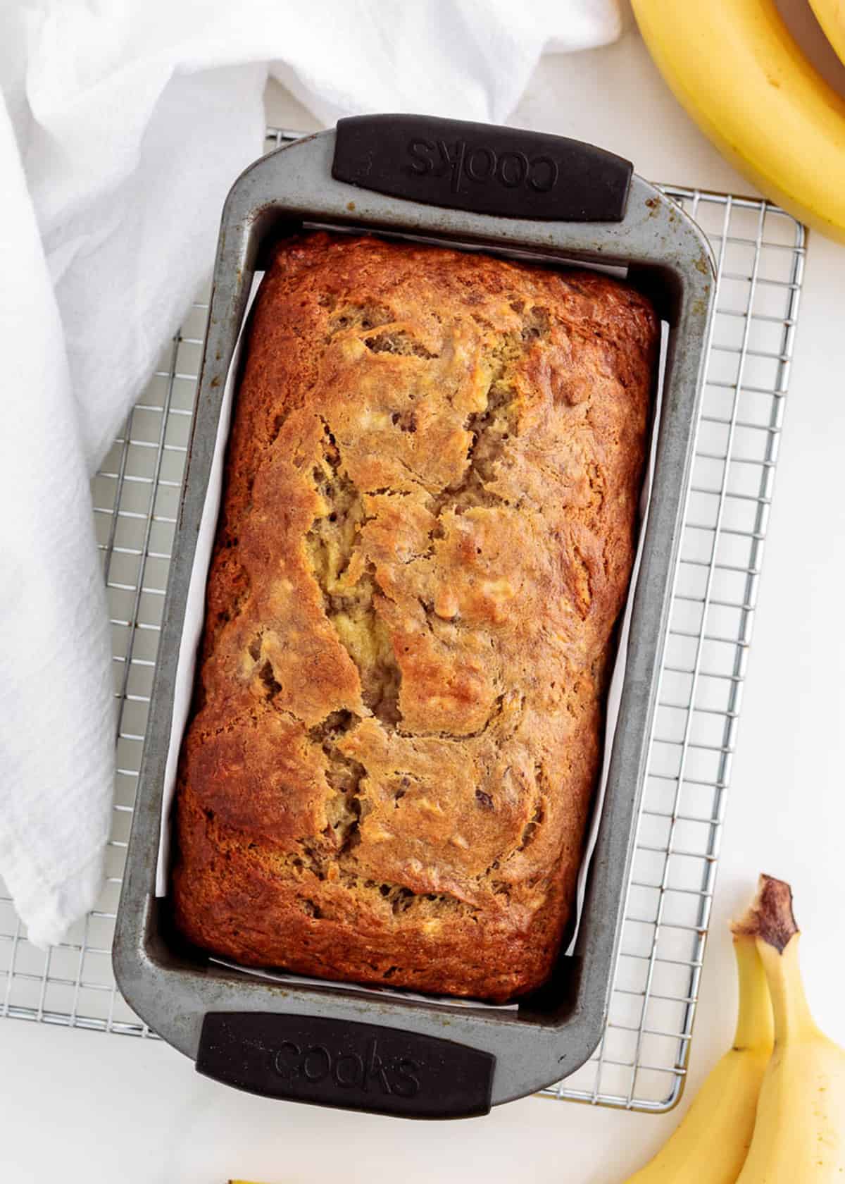 Banana bread in loaf pan on cooling rack.