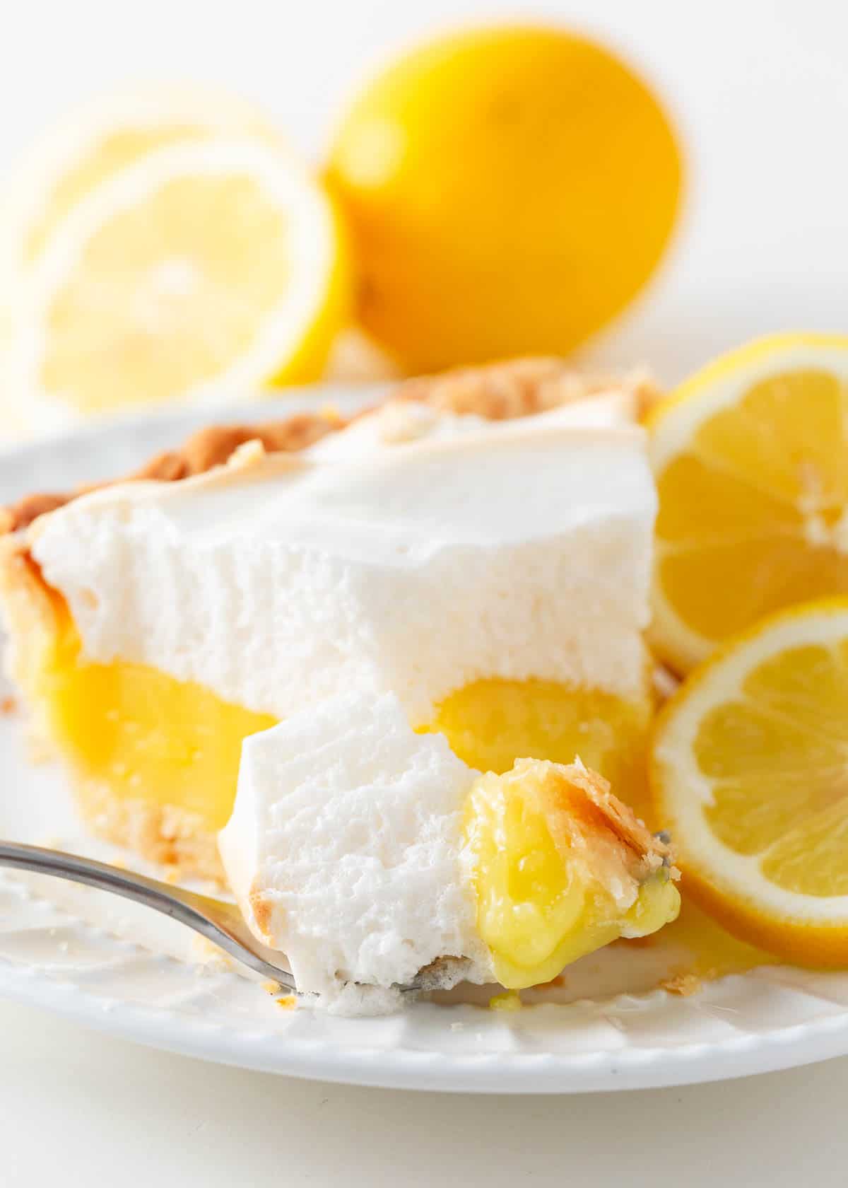 Close up of a slice of lemon meringue pie on a white plate showing vibrant lemon filling and fluffy meringue.