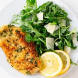 Chicken milanese on a white plate with arugula salad.