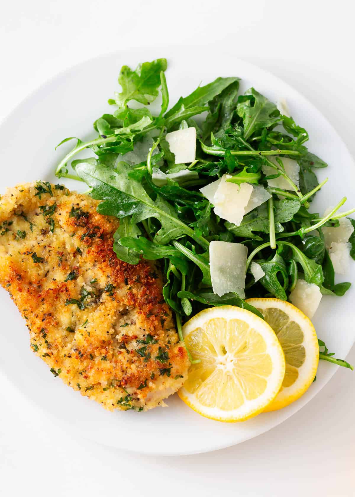 Chicken milanese on a white plate with arugula salad.