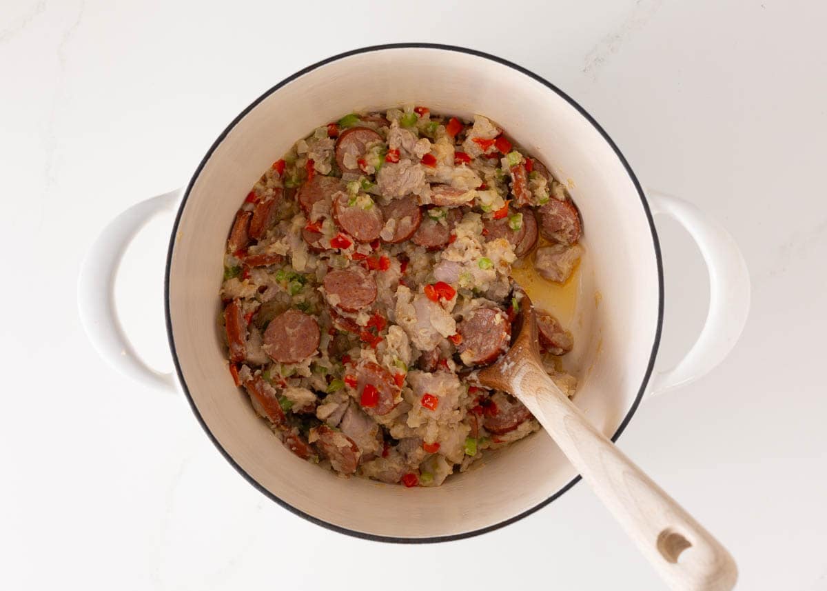 Adding chicken and sausage to a pot with veggies and roux for gumbo.