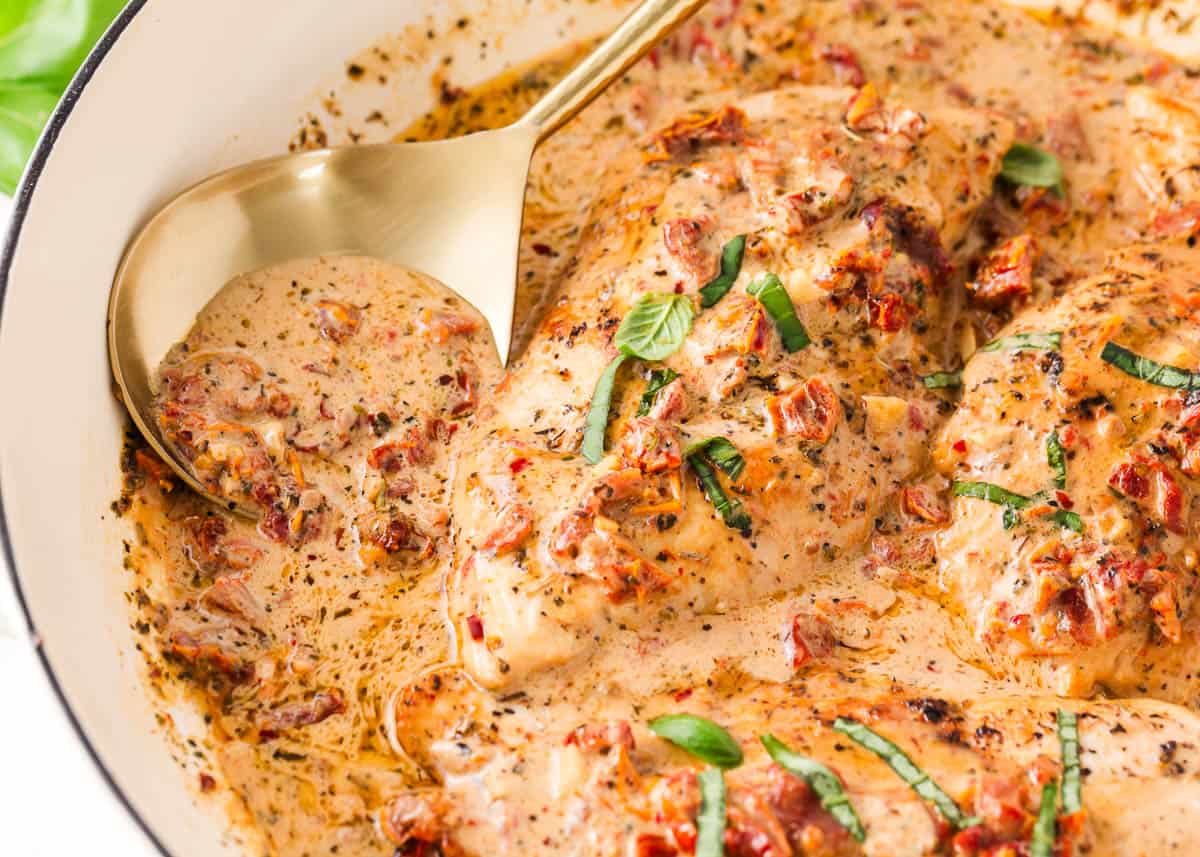 Marry me chicken recipe in a white skillet with a gold serving spoon.