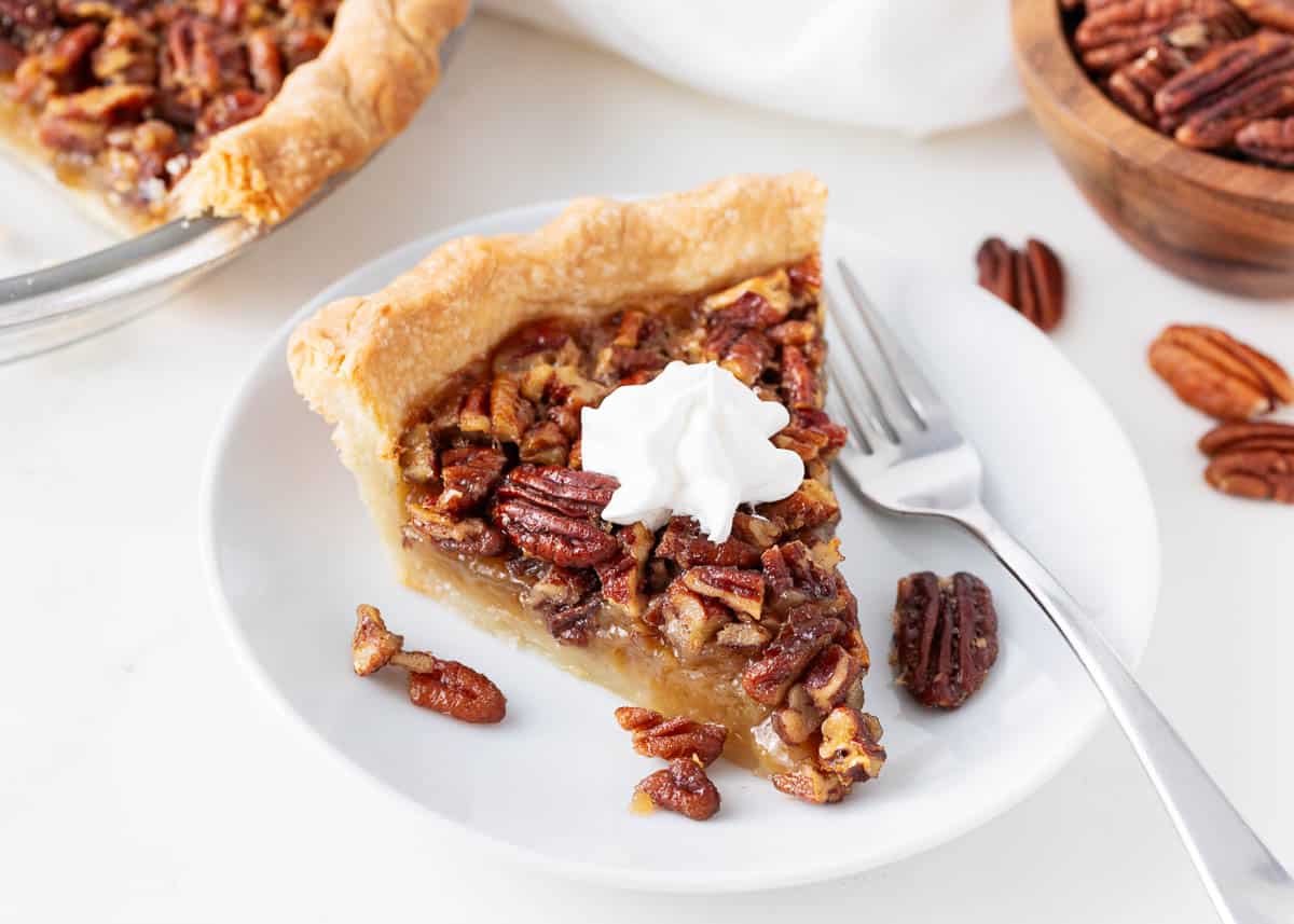 This easy homemade pecan pie is one of my favorite desserts among my Thanksgiving recipes. It's made with a prepared flaky pie crust, a sweet and smooth custard-like filling, and tons of pecans! Slice of pecan pie on a plate.