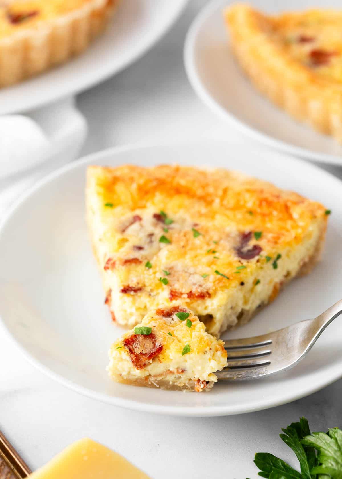 Slice of quiche lorraine on a white plate with fork.