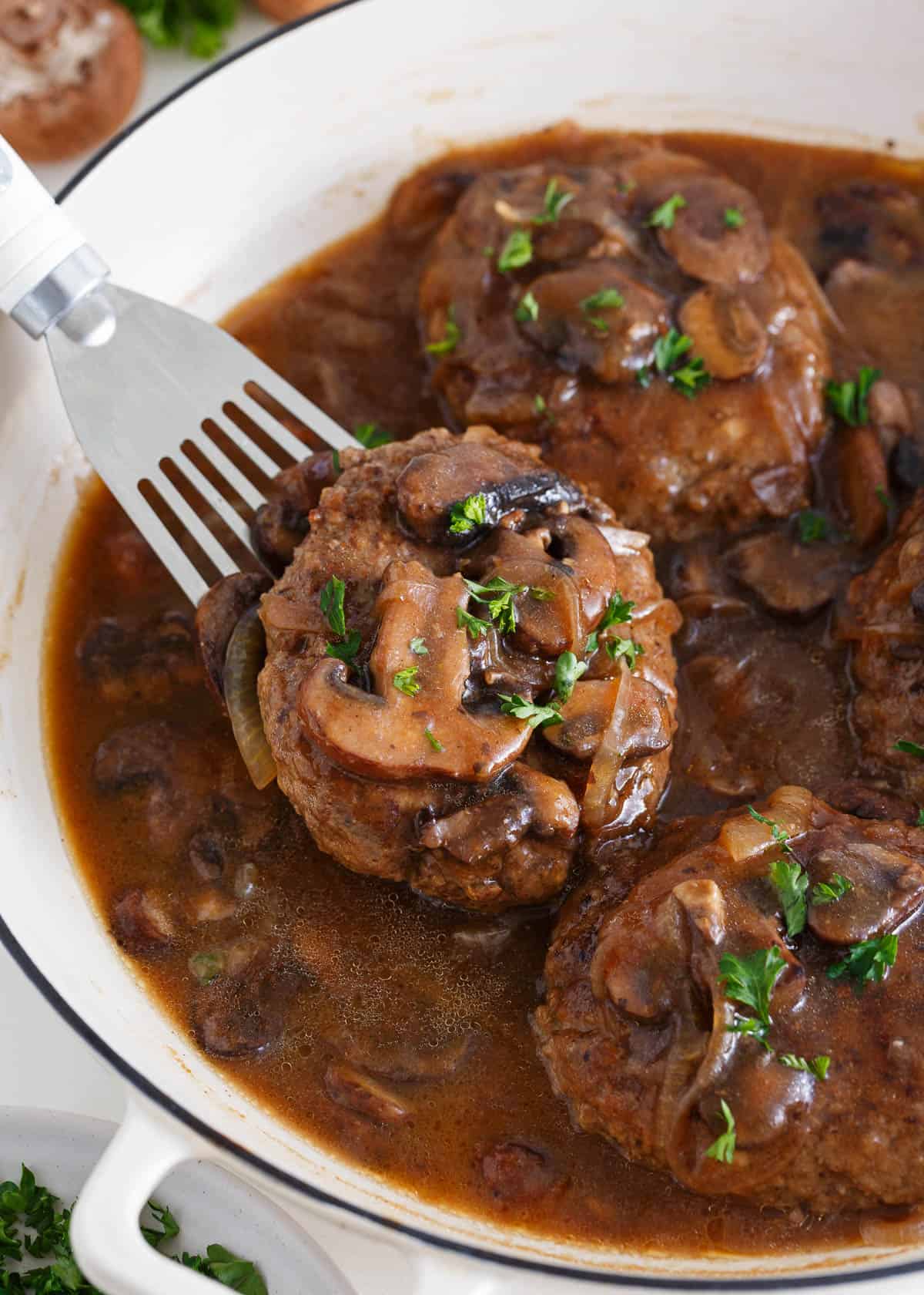 Salisbury steaks in a deep skillet being served with a spatula.