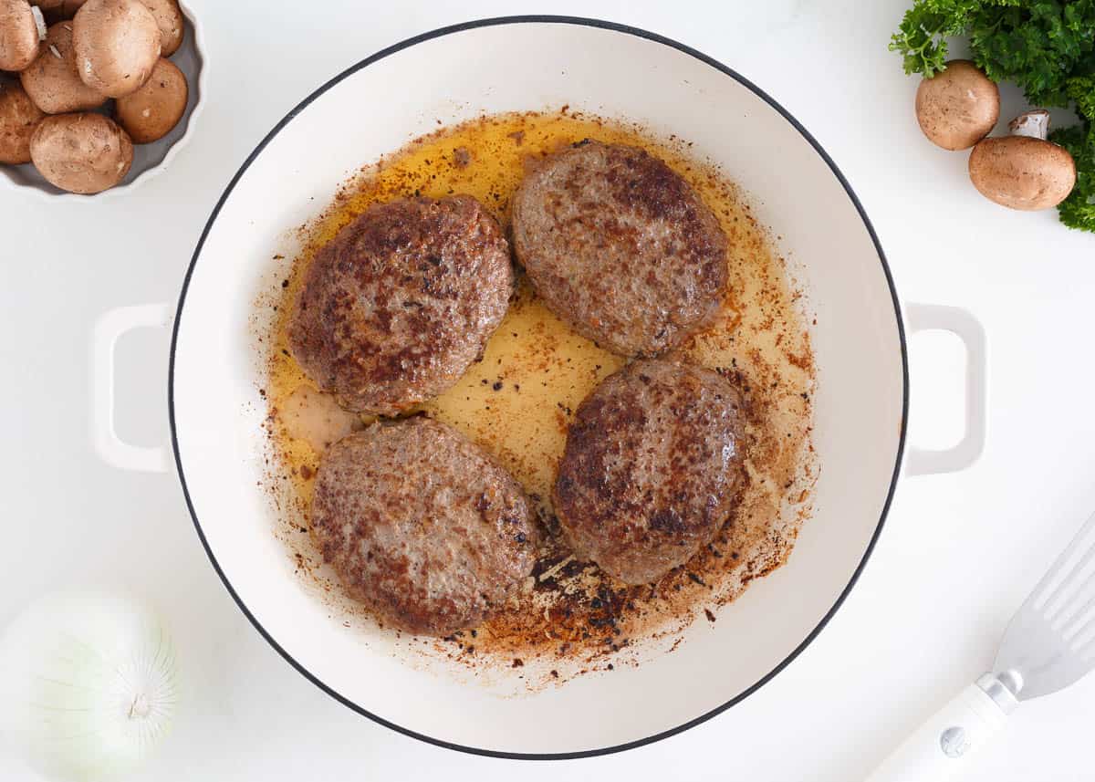 Salisbury steaks cooking in a pot on the stove.