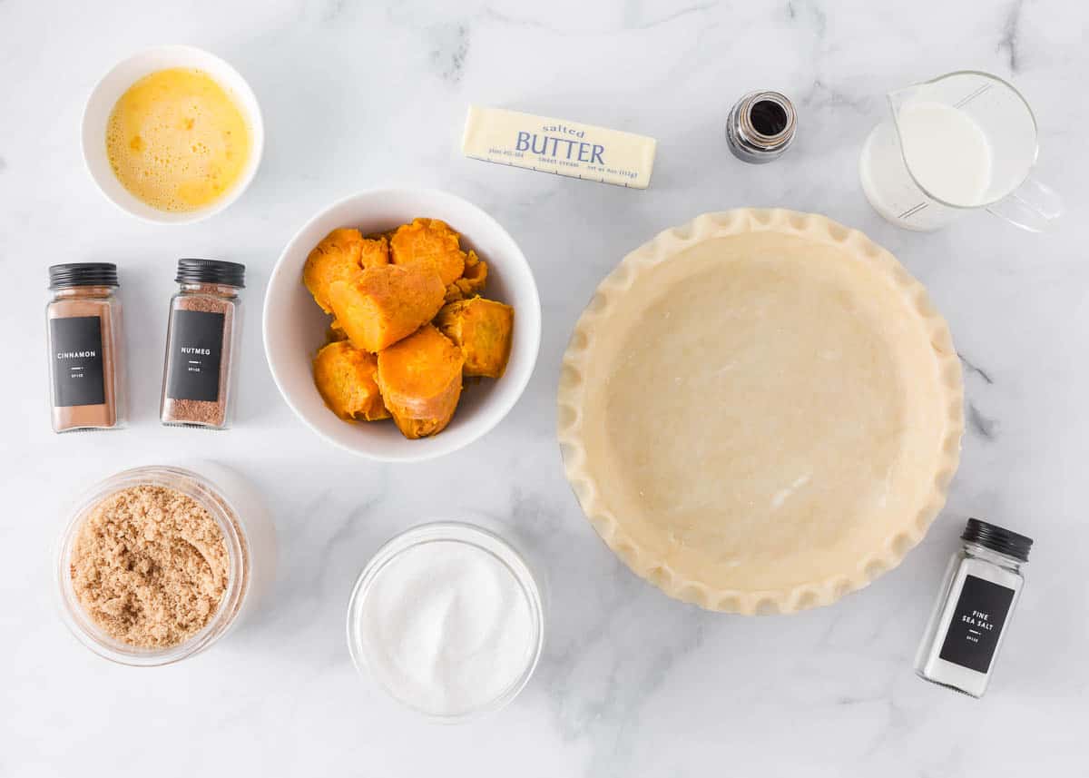 Baked sweet potatoes, pie crust, brown sugar, egs, butter, milk, cinamon, nutmeg and vanilla on the counter.