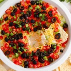 "Taco dip with cream cheese in a white dish with a scoop removed showing the layers, served with tortilla chips.