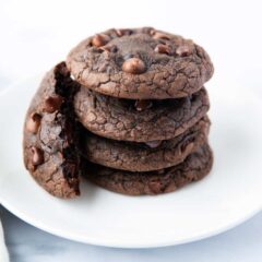 Brownie mix cookies stacked on a white plate with one broken leaning on it's side.