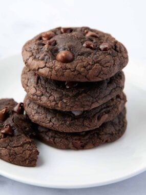 Stack of thick fudgy brownie mix cookies with chocolate chips on a white plate.