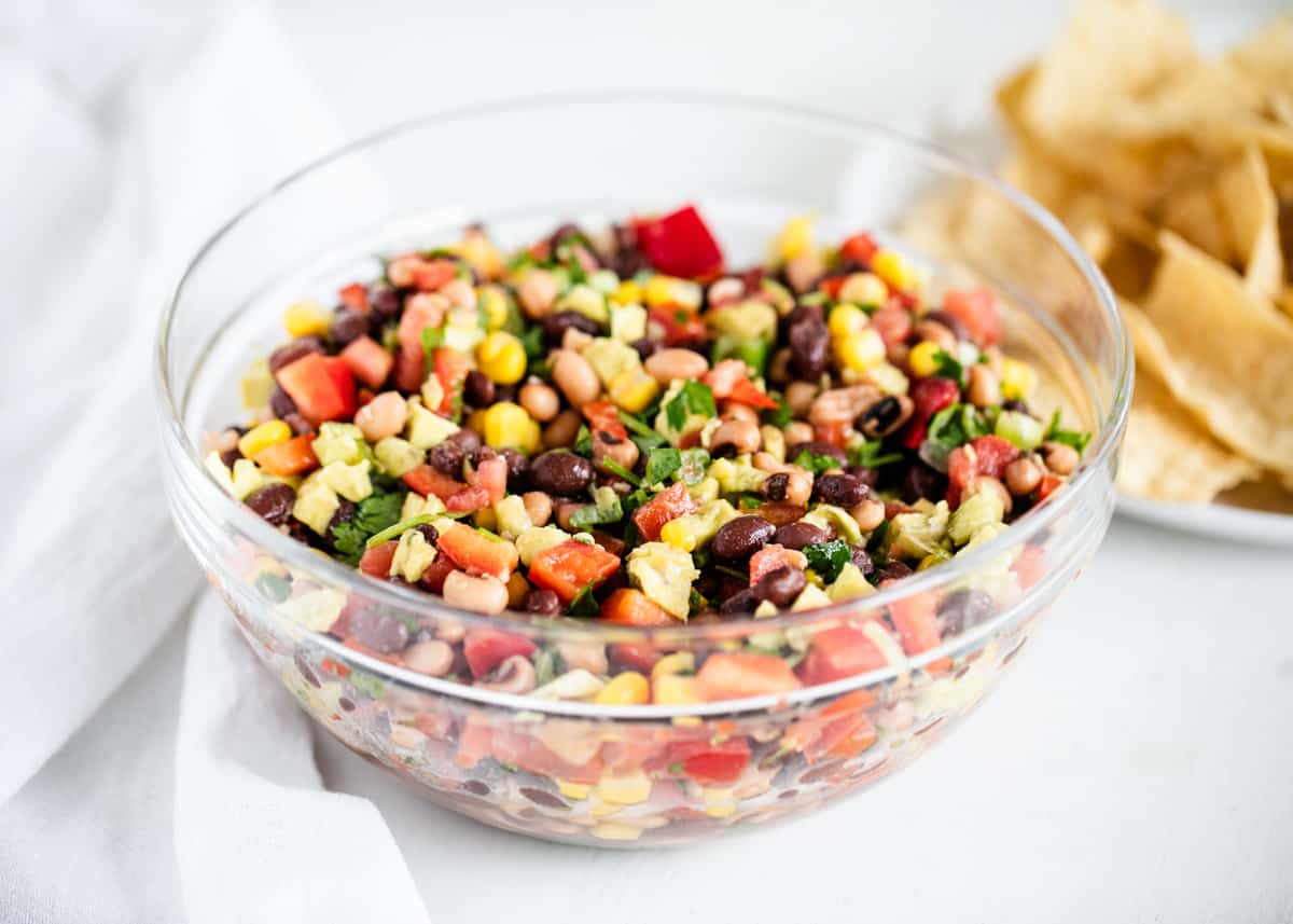 Flavorful and delicious cowboy caviar dip that will become the star of the show at your next get together. Full of fresh veggies and topped with an easy homemade dressing. Cowboy caviar in a glass bowl.