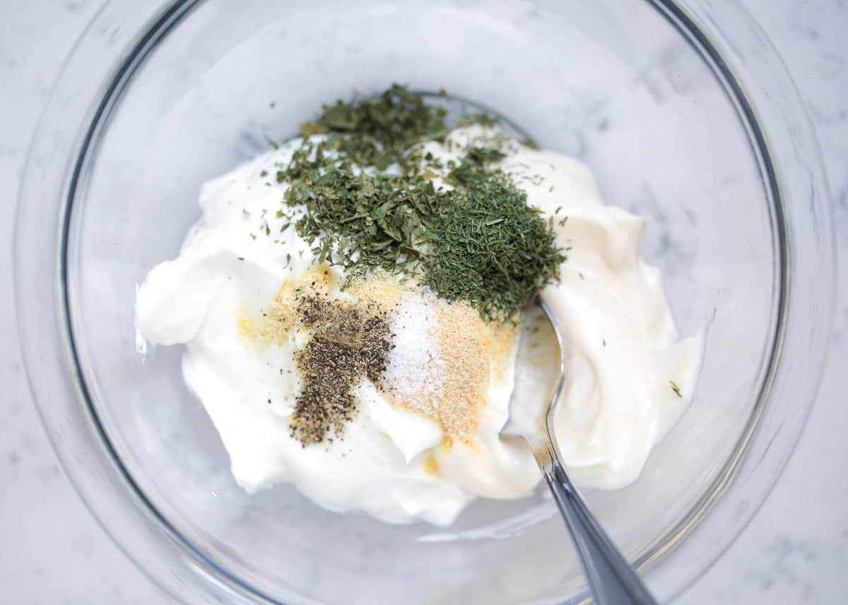 Ingredients for dill dip in a glass bowl with a spoon.