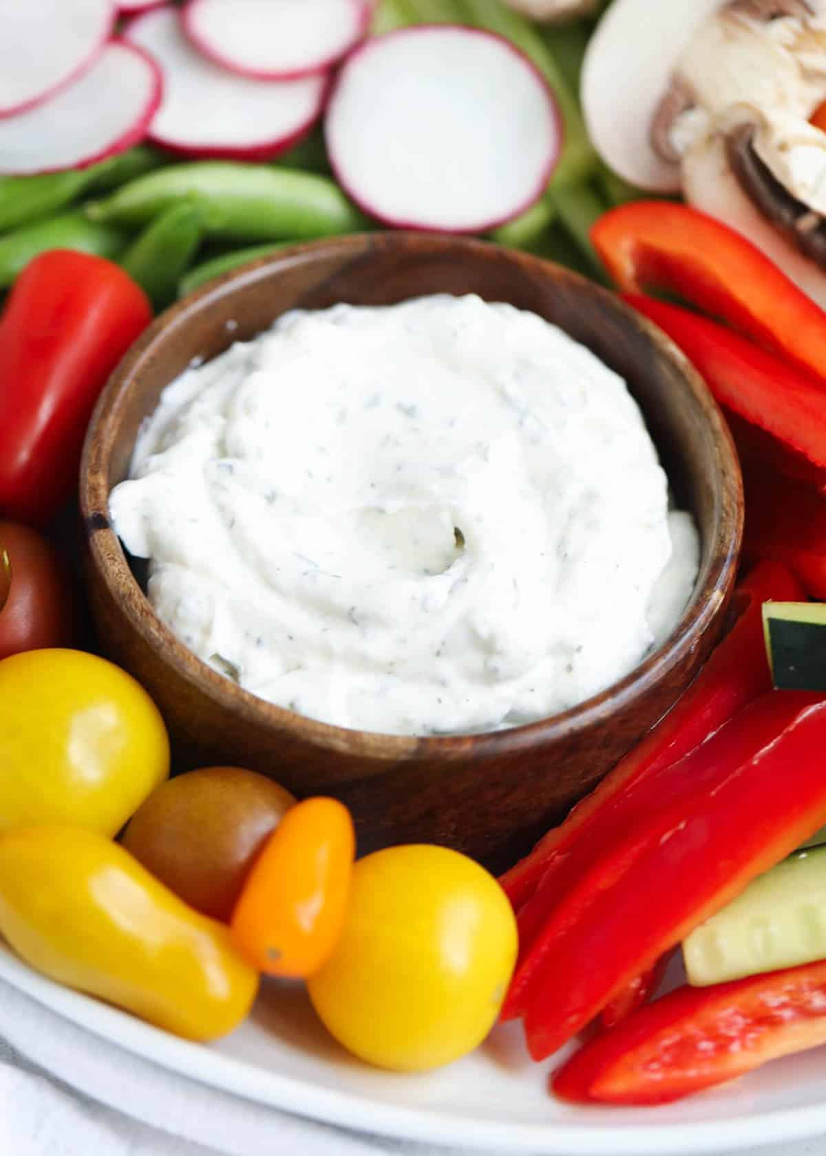 Up close photo of dill dip with vegetables gathered around it. 