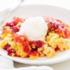 A serving of dump cake on a plate topped with melting vanilla ice cream.