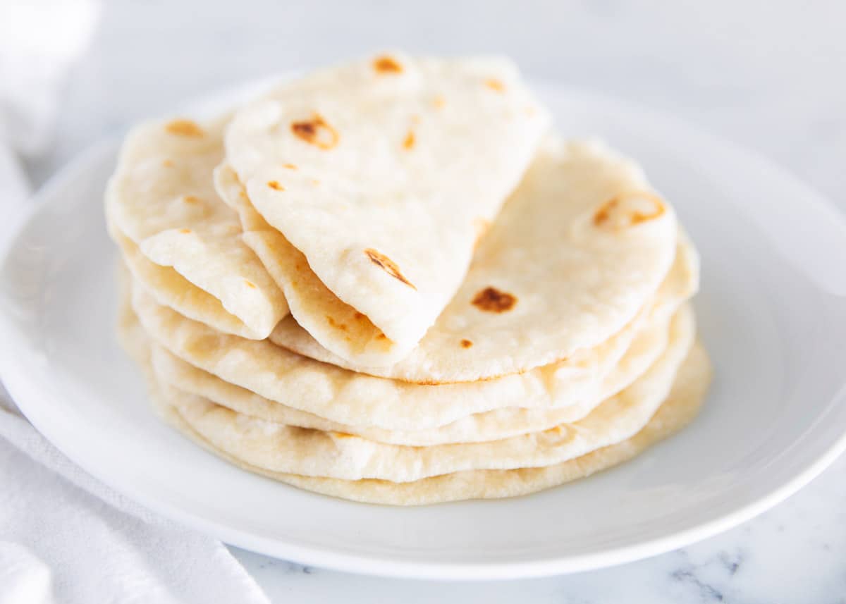 Homemade flour tortillas stacked on top of each other with two rolled together. 