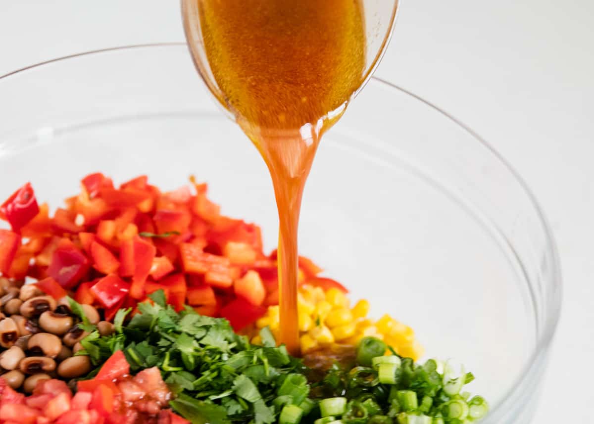 The ingredients in a glass bowl with the dressing being poured over top. 