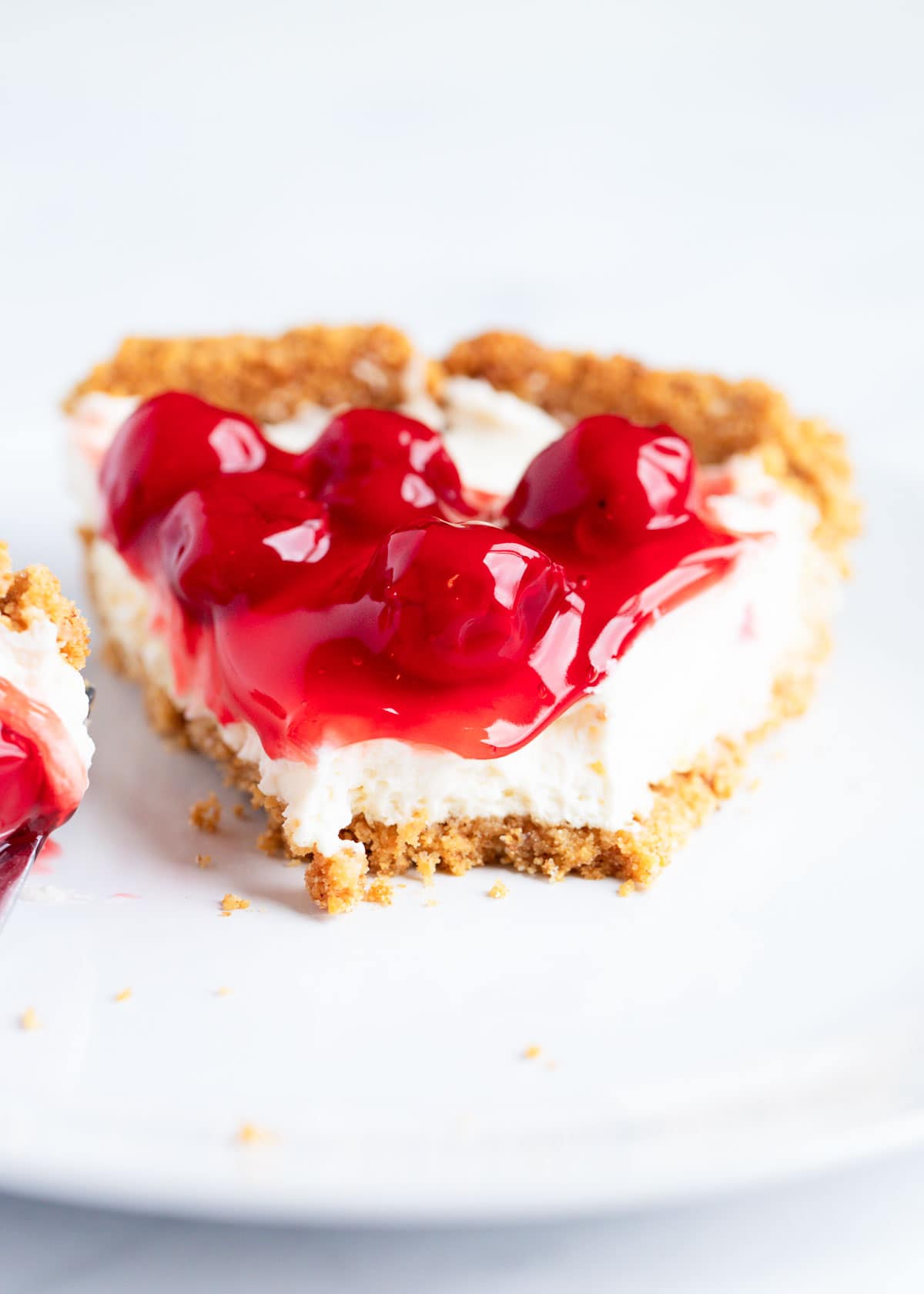 A slice of no bake cheesecake with cherries on top and a bite taken out of the front slice. 