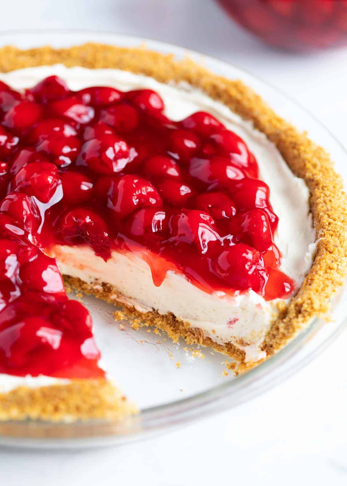 No bake cheesecake with cherry pie filling on top with a slice taken out of it. 