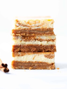Stack of pumpkin cheesecake bars on a white counter.