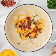 Loaded baked potato soup in a white pot topped with cheese, bacon and chives.
