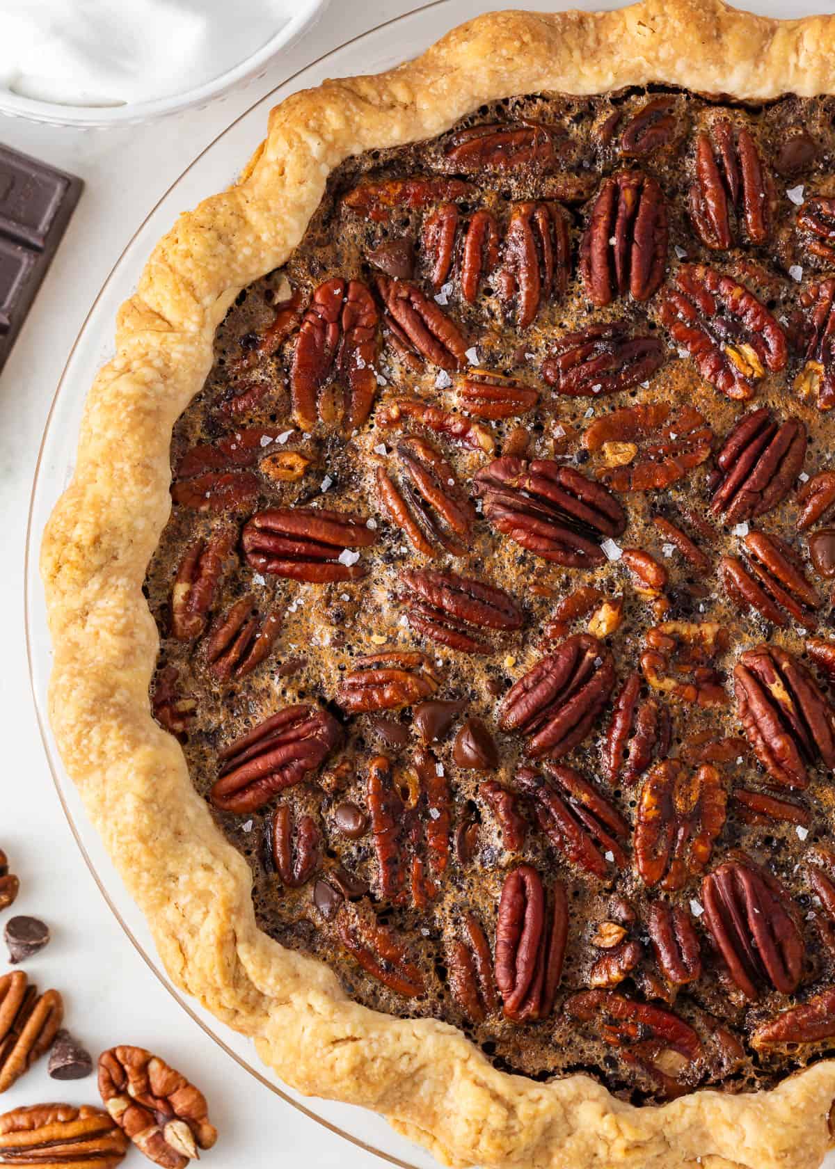 A luscious twist on a classic southern recipe, chocolate pecan pie is rich, velvety, and chocolatey loaded with pecans and topped with chocolate shavings and whipped cream. This is a decadent dessert you’ll want to show off! Close up of chocolate pecan pie.
