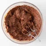Mixing chocolate frosting in a glass bowl.