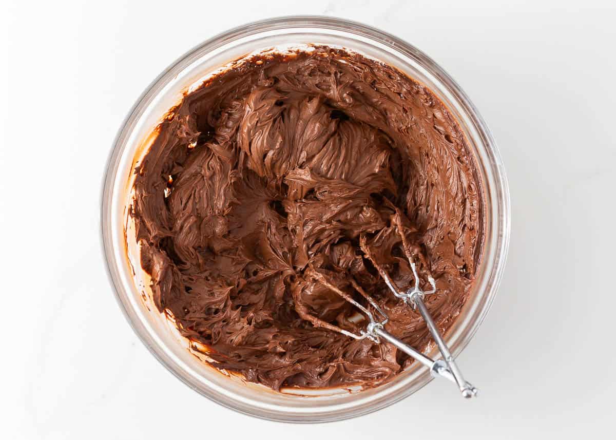 Mixing chocolate frosting in a glass bowl.