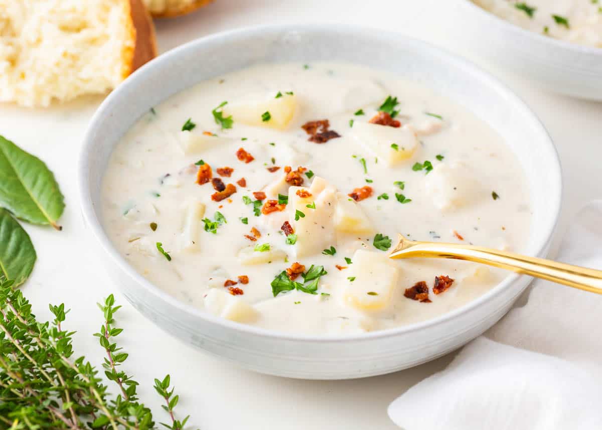 Curl up and indulge in the most comforting bowl of soup you’ll ever make. Every bite of this clam chowder recipe is thick and smooth and when you make it with real clams, you can't help but feel like you're sitting in New England! Clam chowder in a white bowl.