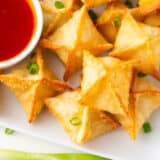 Crab rangoon on a plate with sauce.