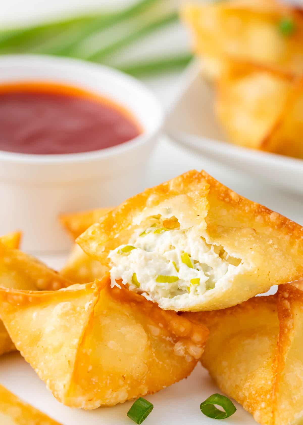 Crab rangoon with a bite taken on a plate with sauce.