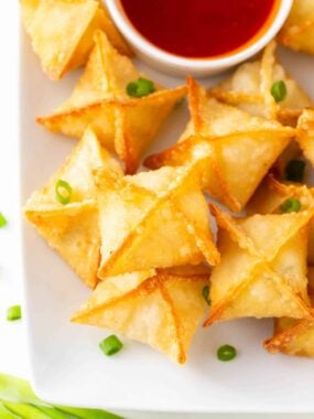 Crab rangoon on a plate with sweet and sour sauce.