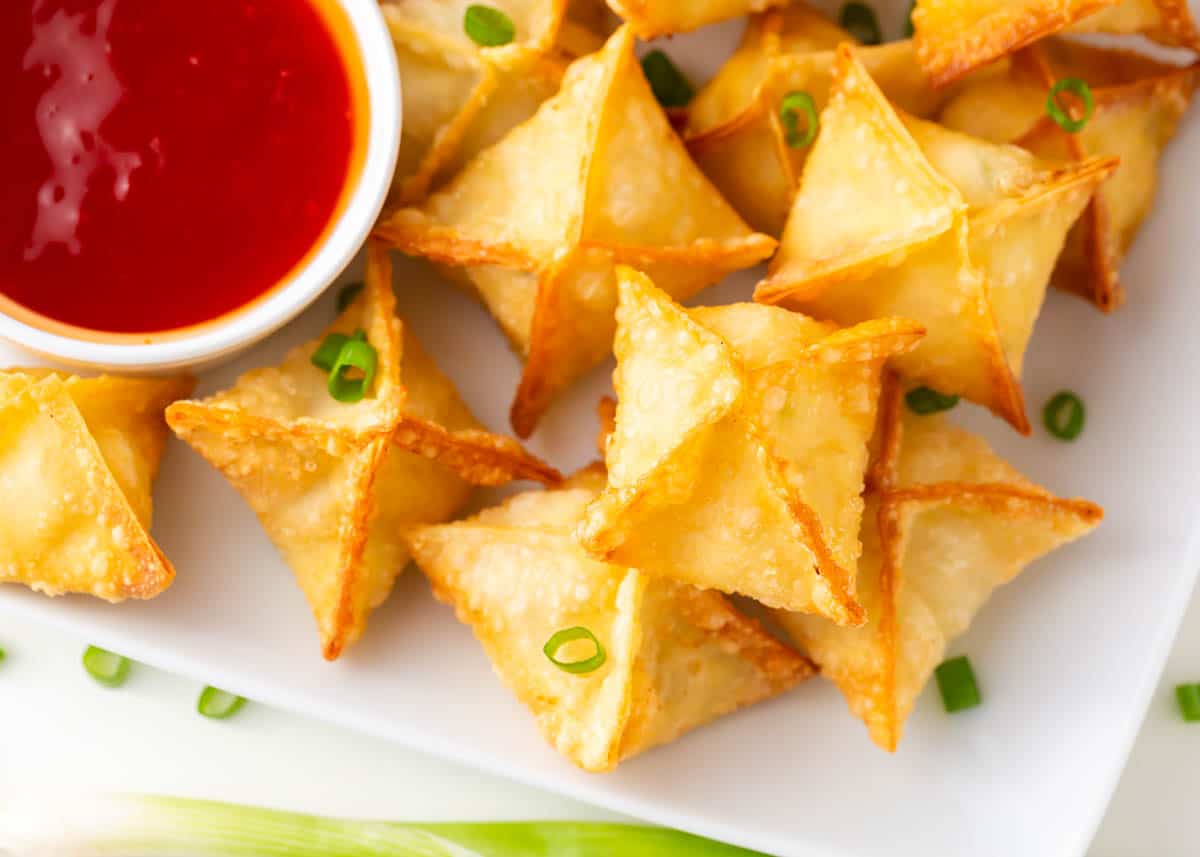 Crab rangoon on a plate with sauce.