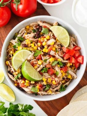 Slow cooker Mexican chicken with black beans and corn served in a white bowl, ready to be added to tacos or rice bowls.