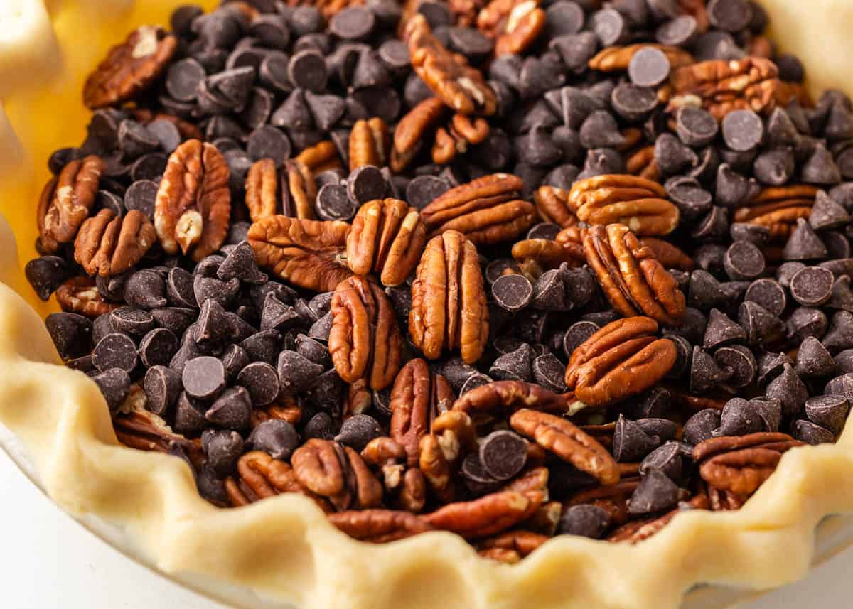 A luscious twist on a classic southern recipe, chocolate pecan pie is rich, velvety, and chocolatey loaded with pecans and topped with chocolate shavings and whipped cream. This is a decadent dessert you’ll want to show off! Showing how to make chocolate pecan pie.