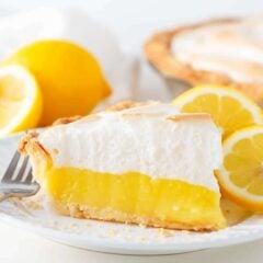 Slice of homemade lemon meringue pie with bright lemon filling, fluffy meringue topping, and lemon slices on a plate.