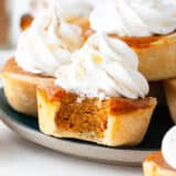 Mini pumpkin pies with a bite taken on plate.