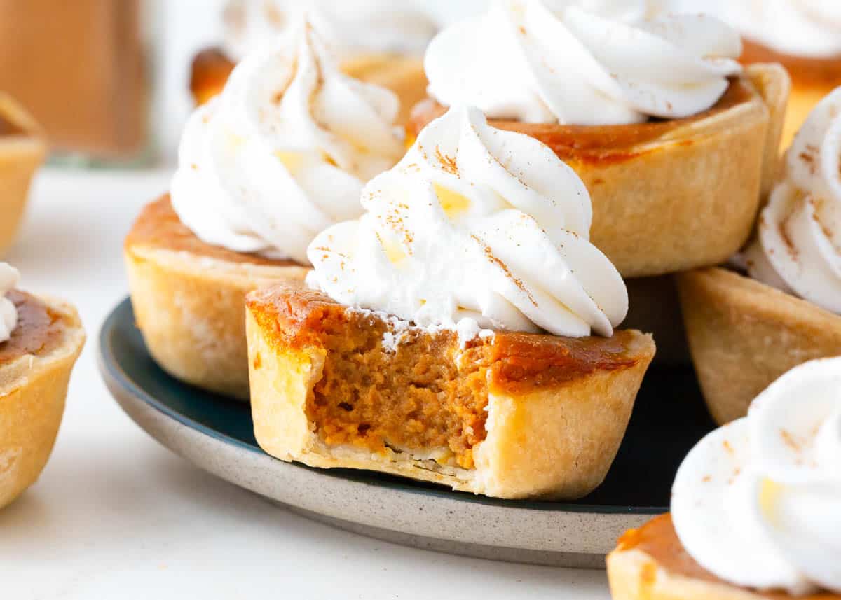 Mini pumpkin pies with a bite taken on plate.