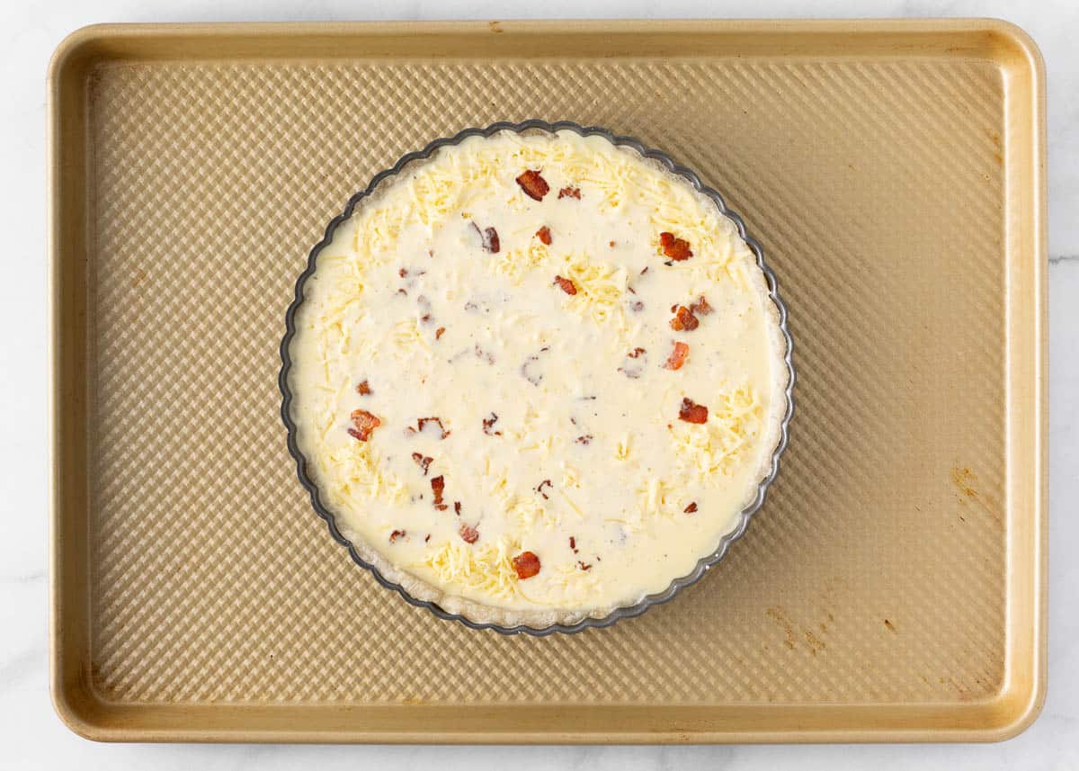 Unbaked quiche lorraine in pie crust on baking sheet. 