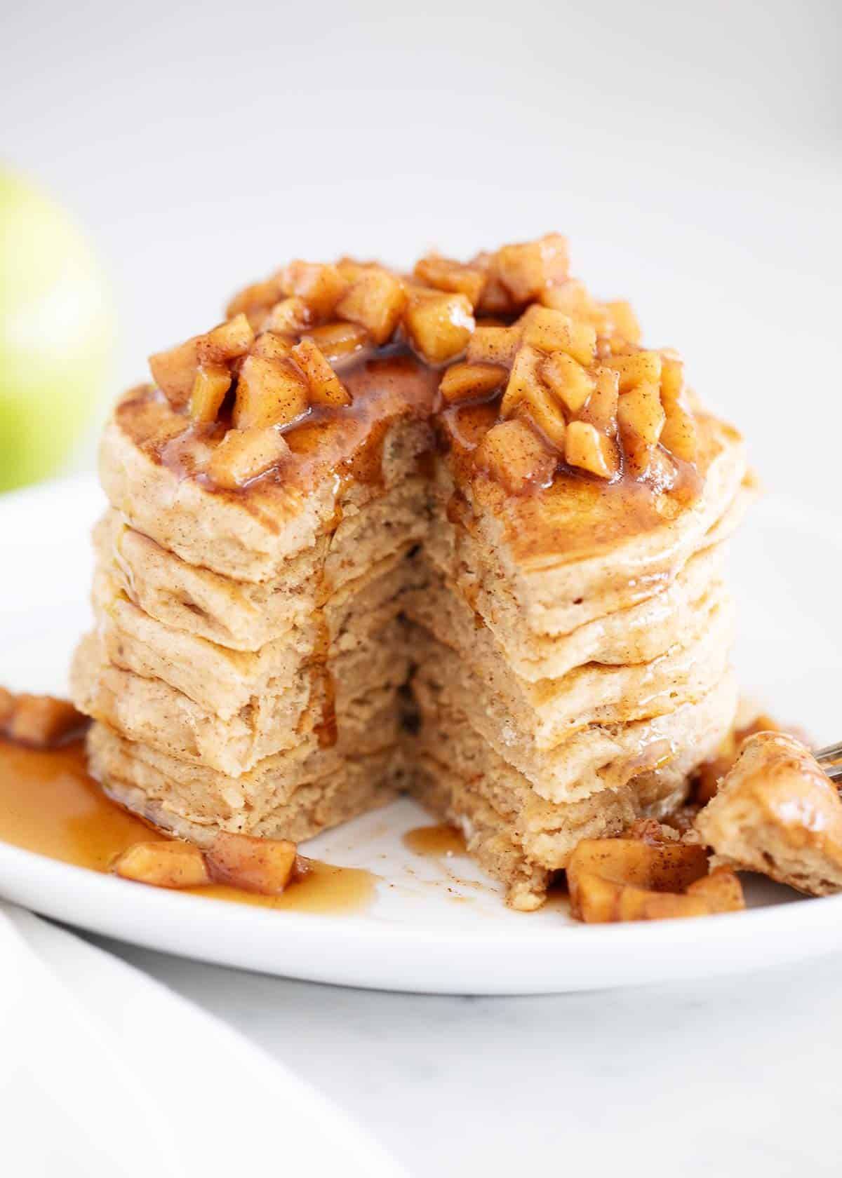 Stack of apple cinnamon pancakes with a triangle wedge cut out of the stack. 